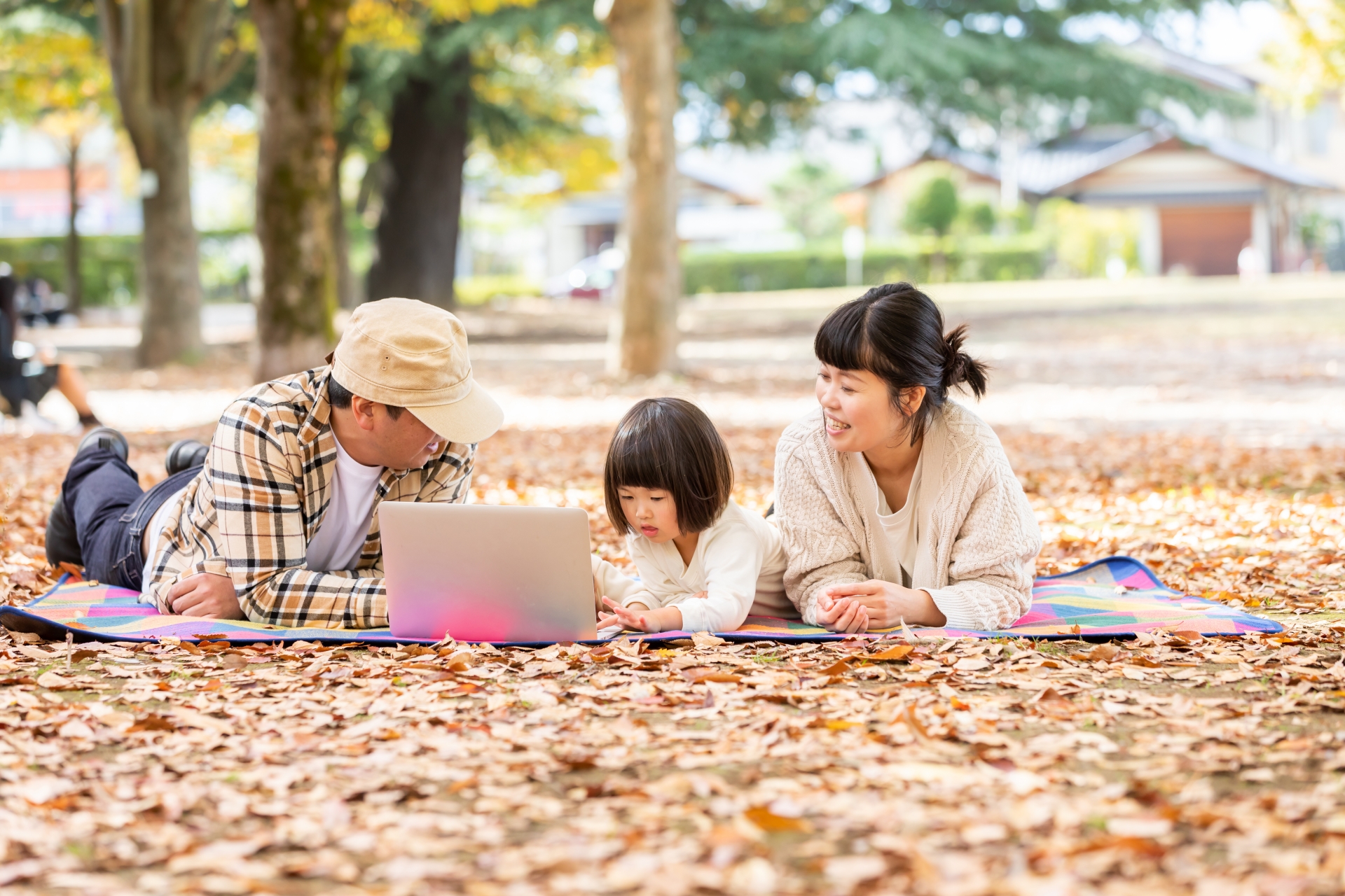 秋の公園で家族が寝ころびながらPCを見ている