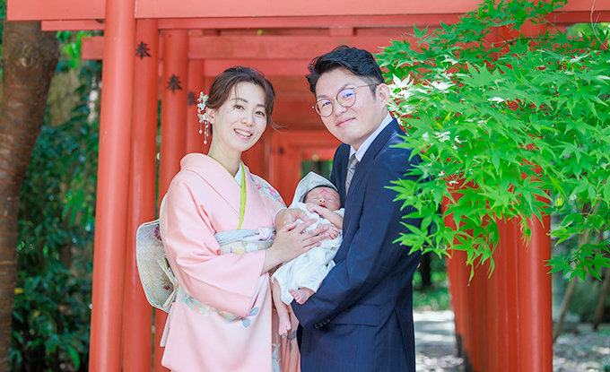 五條市御霊神社本宮の赤い鳥居が連なる前でお宮参りを済ませた夫婦が男の子を抱いて微笑んでいる