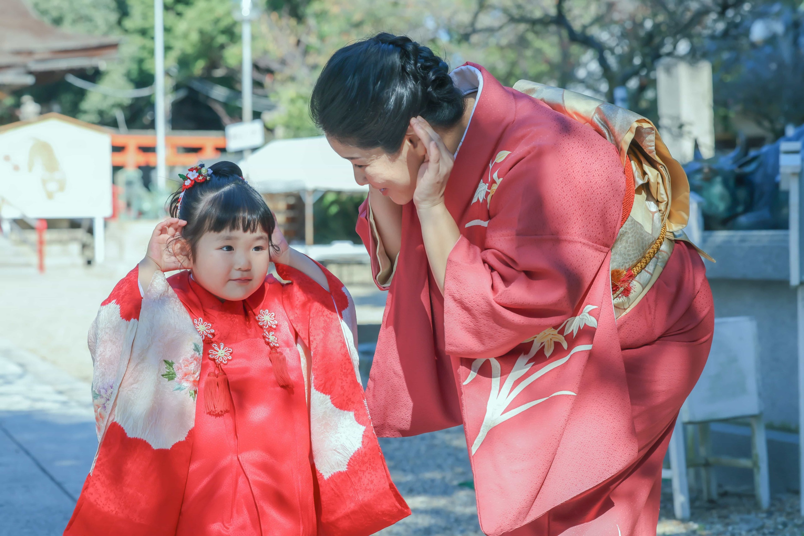 七五三参り　赤い和装の３歳女の子と赤い和装の母が耳に手を添えてよく聞こえる様に