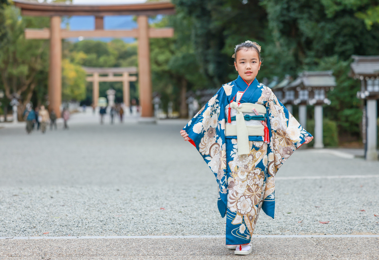 橿原神宮の参道で、緑色の和装で七五三参りをした女の子が鳥居をバックに袖を持ってポーズ