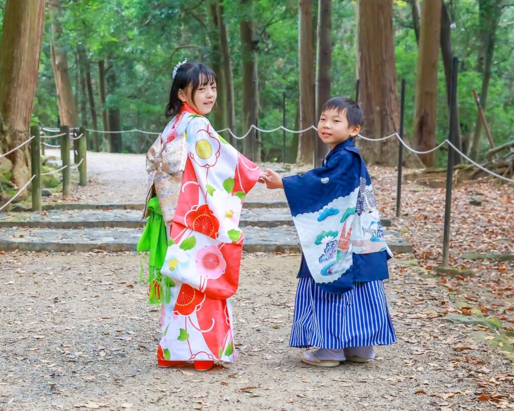 春日大社の参道で、七五三参りの和装をした７歳の女の子と５歳の男の子が手を繋いで笑顔で振り向く様