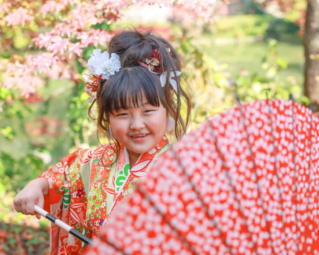 高鴨神社で七五三参りをした女の子が赤い和傘を広げて笑顔の様子