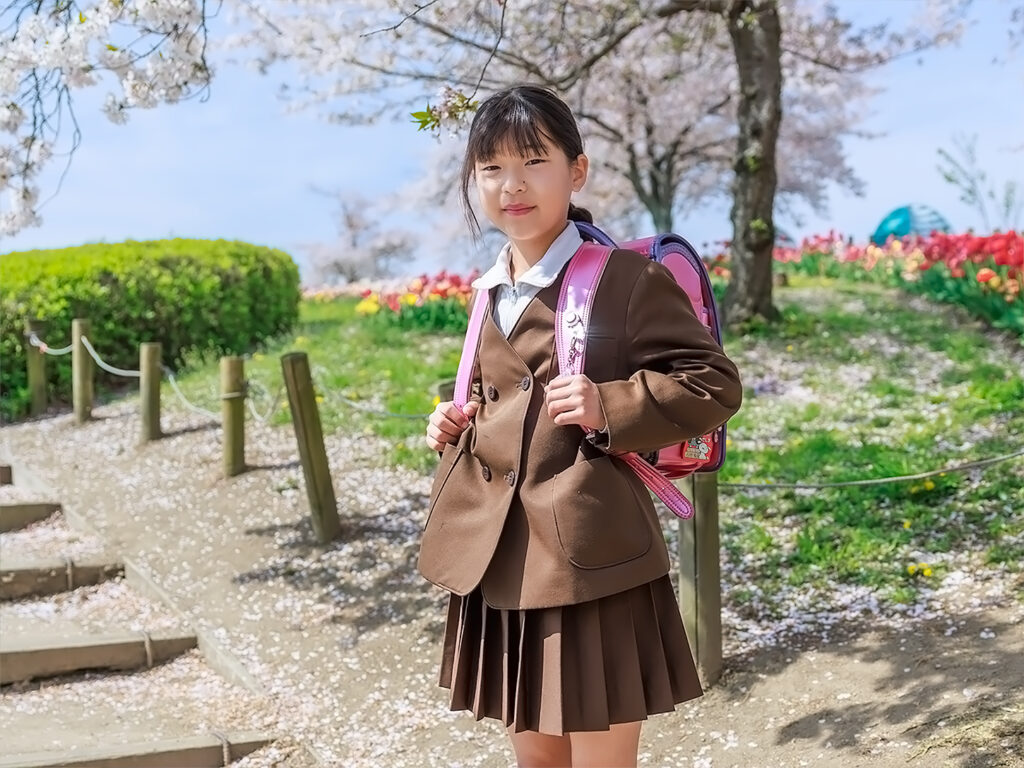 桜が咲く馬見丘陵公園で4姉妹の新生活記念撮影-新小校生の四女が新入学の制服にランドセルを背負い微笑む様