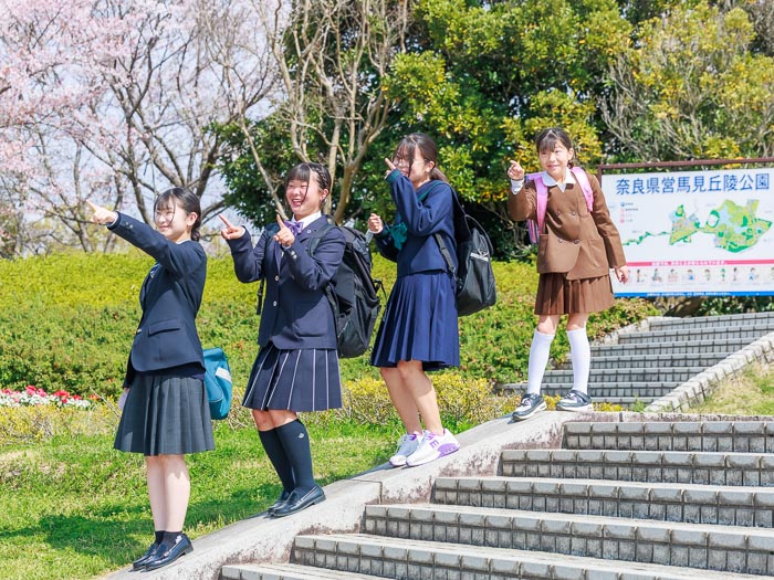 桜が咲く馬見丘陵公園で新入学の制服を着た4姉妹が階段に縦一列に並びそれぞれポーズをとっている