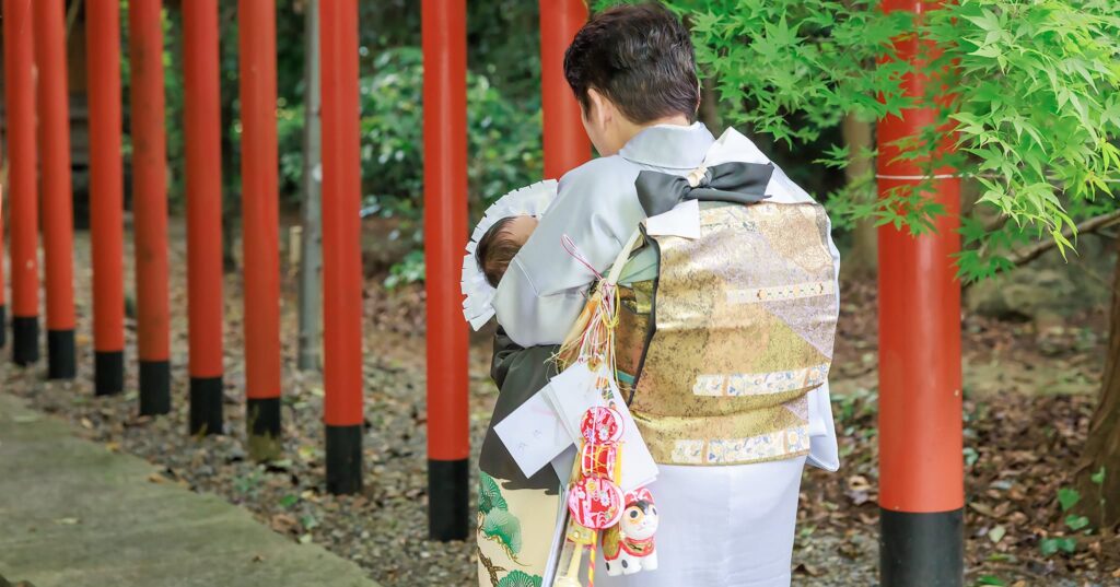 御霊神社本宮でお宮参りをした男の子が祖母に抱かれての赤い鳥居を潜る様
